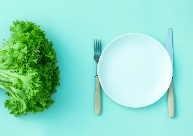 Vue de dessus salade verte fraîche, chou, assiette vide blanche, fourchette, couteau sur fond vert, espace copie