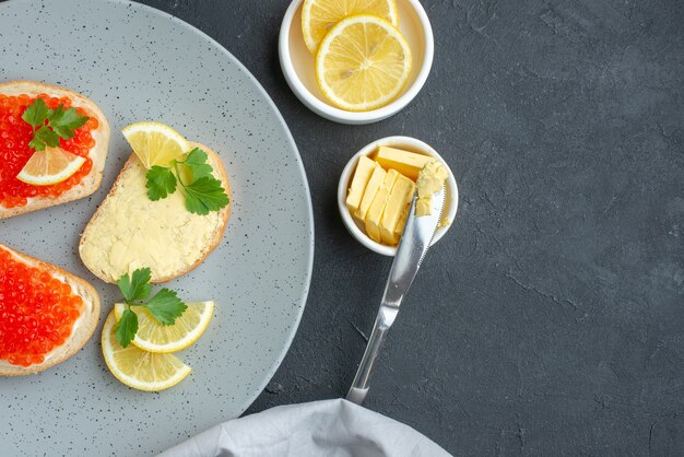 vue de dessus des sandwichs au caviar avec du citron et des couverts à l'intérieur d'une assiette bleue sur une surface sombre