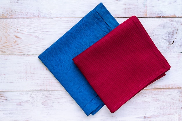 Vue de dessus des serviettes en tissu de couleurs bleus et bordeaux sur fond blanc rustique.