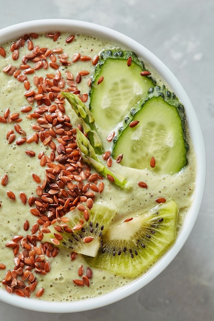 Vue de dessus d'un smoothie vert d'asperges kiwi concombre avec graines de lin dans un bol blanc sur fond gris