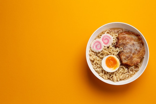 Vue de dessus de la soupe de nouilles japonaises ramen dans un bol blanc avec nouilles, bouillon de viande, porc rôti en tranches, narutomaki, œuf avec jaune sur fond orange vif. Plat traditionnel du Japon, espace pour le texte