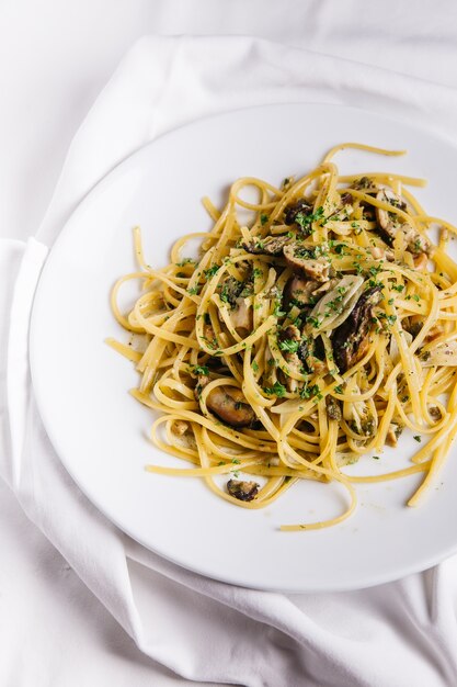 Vue de dessus des spaghettis aux huîtres servis dans une assiette blanche sur une nappe blanche.