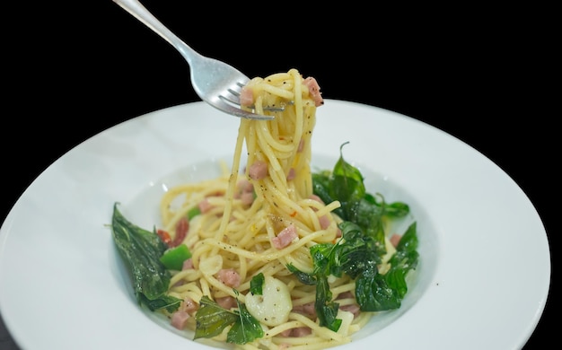 Vue de dessus des spaghettis carbonara avec fourchette sur plat blanc sur fond noir focus sélectif