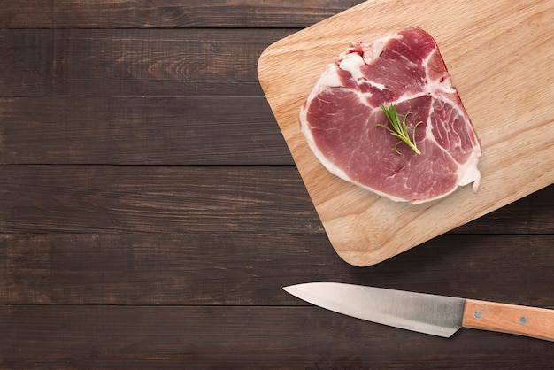 Vue de dessus steak de porc cru sur une planche à découper et un couteau sur fond de bois. Copyspace pour votre texte