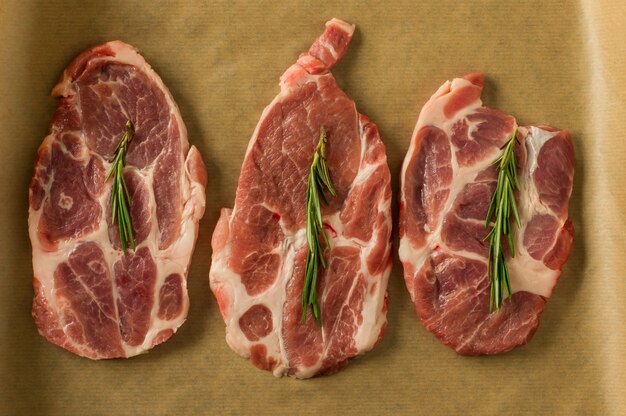 Vue de dessus des steaks de porc frais hachés au romarin sur du papier sulfurisé prêt à cuire. Cuisine et culinaire.