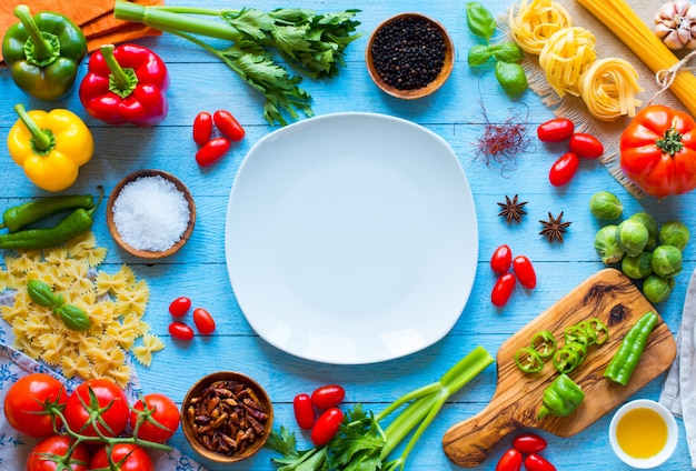 Vue de dessus d'une table en bois pleine d'ingrédients de pâtes italiennes comme les poivrons, les tomates, l'huile d'olive, le basilic