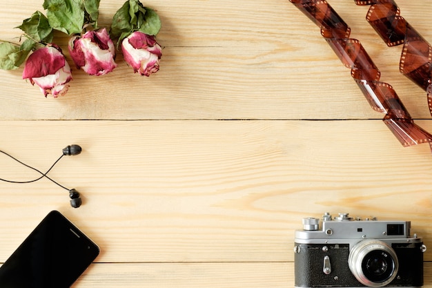 Vue de dessus de la table en bois avec smartphone, casque, appareil photo vintage, film et roses séchées avec des feuilles
