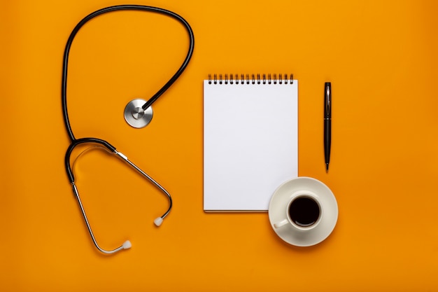 Vue de dessus de la table de bureau de médecin avec stéthoscope, café et papier vierge sur le presse-papiers avec stylo. Vue de dessus avec espace de copie, pose à plat