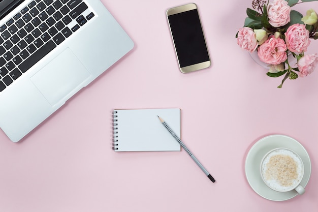 Vue de dessus de la table de bureau rose avec ordinateur portable, smartphone, tasse de café et de fleurs. Espace de copie, pose à plat.