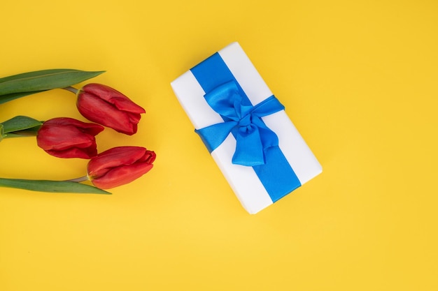 Vue de dessus de la table jaune avec boîte-cadeau avec ruban bleu et tulipes