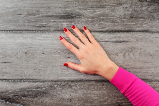 Vue de dessus de table sur la main droite de la jeune femme avec des ongles rouge foncé sur un bureau en bois gris vide.