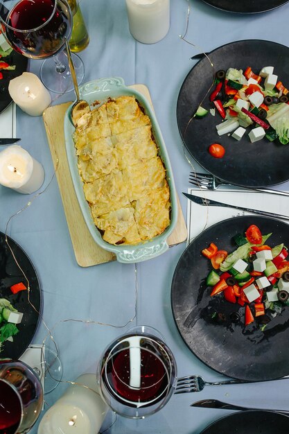 Vue de dessus d'une table à manger avec des salades, du vin rouge, des pommes de terre cuites et des bougies prêtes pour la célébration de Noël.