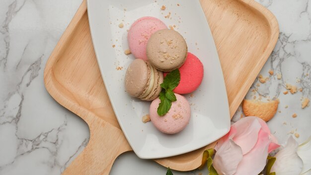 Vue de dessus de la table en marbre avec une assiette de macarons colorés français sur plateau en bois décoré de fleurs