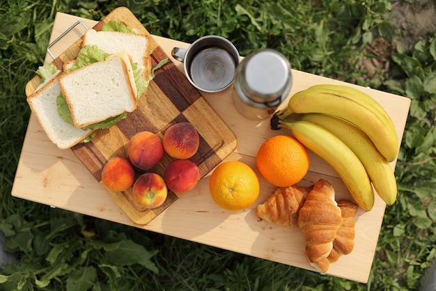 Vue de dessus de la table avec de la nourriture en plein air thermos bananes fraîches pêches oranges et sandwichs sur la table dans un camp touristique