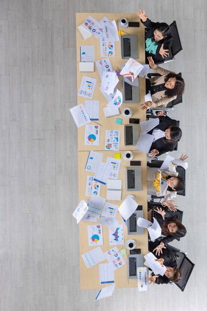 Vue de dessus de table de six femmes d'affaires asiatiques assises en ligne droite sur une table de conférence en bois et jetant des tableaux et des graphiques en l'air au bureau. Concept pour réunion d'affaires.