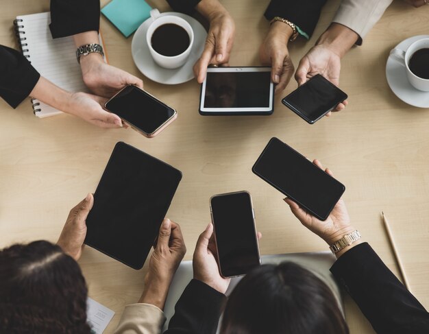 Vue de dessus de table d'une table de conférence en bois avec six mains de femmes d'affaires tenant des téléphones intelligents et des tablettes autour de la table. Concept pour réunion d'affaires.