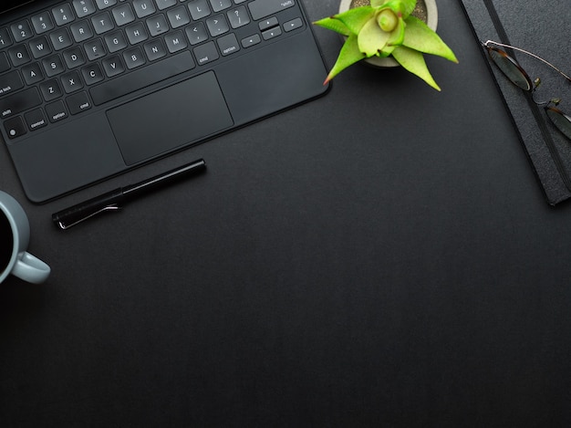 Vue de dessus de la table de travail avec clavier d'ordinateur portable, stylo, ordinateur portable, pot de fleurs et espace de copie dans la salle de bureau à domicile