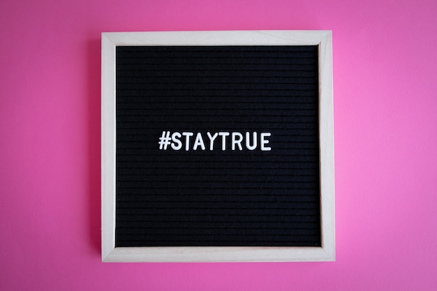 Vue de dessus d'un tableau noir avec un cadre blanc avec un hashtag staytrue sur fond rose