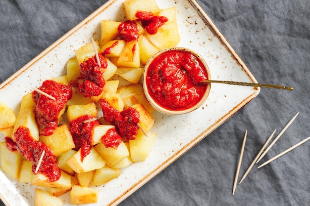 Vue de dessus sur les tapas traditionnelles de la cuisine espagnole Patatas Bravas Pommes de terre frites avec sauce tomate chaude dans un plat en céramique servi avec des cure-dents