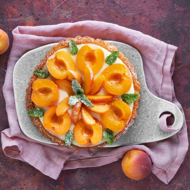 Vue de dessus de la tarte aux abricots avec des feuilles de menthe sur une planche en céramique sur un mur sombre