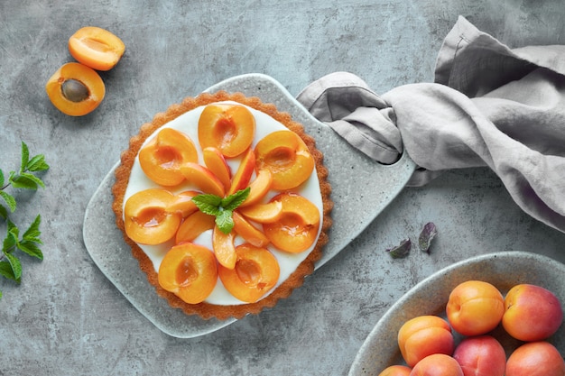 Photo vue de dessus de la tarte aux abricots avec des feuilles de menthe sur une table texturée grise.