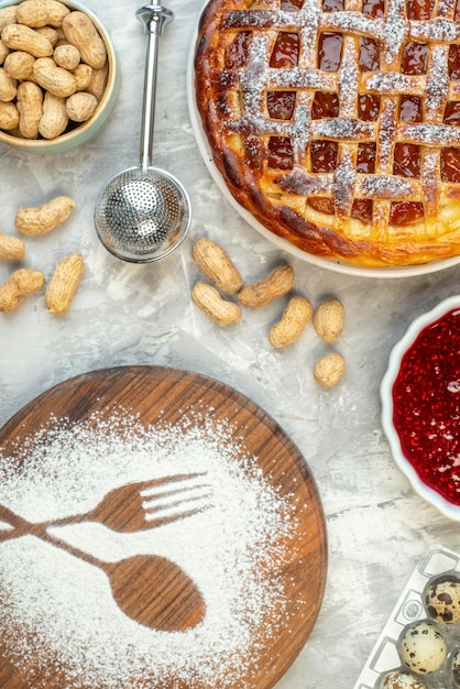 Vue de dessus tarte avec confiture sur assiette autres choses dans des bols empreinte fourchette et cuillère en farine sur table