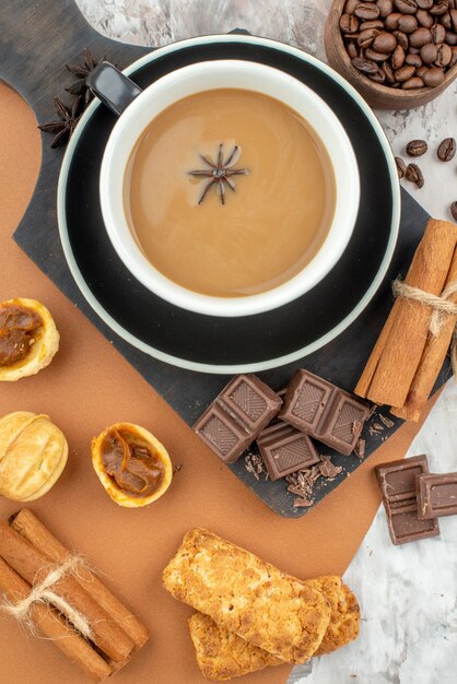 vue de dessus tasse de café à l'anis chocolat bâtons de cannelle cookies sur planche de bois grains de café torréfiés dans un bol en bois sur la table