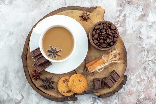 vue de dessus tasse de café avec biscuits à l'anis grains de café torréfiés dans un bol en bois bâtons de cannelle au chocolat attachés avec de la corde anis sur planche de bois rustique sur table