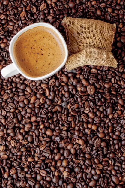 Vue de dessus de la tasse de café avec sac de café sur les grains de café