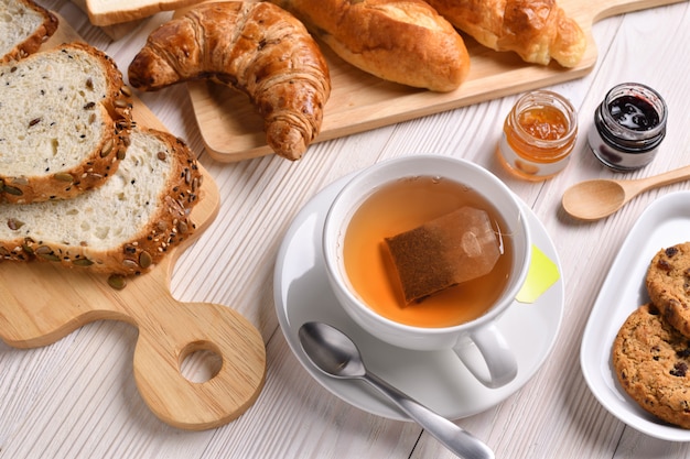 Vue de dessus de la tasse de thé avec du pain ou du pain, des croissants et de la boulangerie sur une table en bois blanc