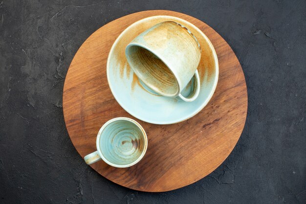 Vue de dessus des tasses et soucoupes colorées douces sur une planche à découper ronde brune sur fond noir avec espace libre