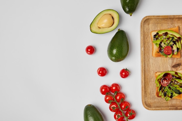 Vue de dessus des toasts sur une planche à découper en bois avec des avocats et des tomates cerises sur fond gris