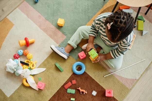 Photo vue de dessus d'un tout-petit noir jouant avec des jouets colorés sur un tapis confortable à la maison dans la chambre des enfants