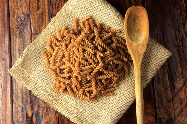 Vue de dessus de toute la masse de Fusilli, sur une serviette rustique en tissu avec une cuillère en bois, sur un fond en bois. espace de copie