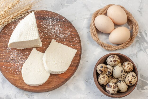 vue de dessus tranches de fromage blanc sur planche de bois oeufs de poule oeufs de caille dans un bol épis de blé sur table