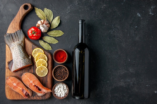 vue de dessus tranches de poisson frais avec assaisonnements et bouteille de vin sur fond sombre repas de poisson salade fruits de mer eau fruits de mer viande océan