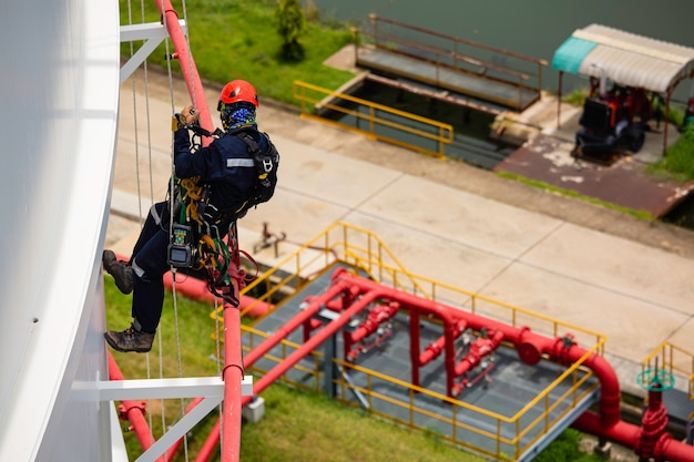 Vue de dessus les travailleurs masculins contrôlent la corde vers le bas du réservoir, l'inspection de l'accès à la corde de l'épaisseur du réservoir de stockage de la plaque de coque, le travail de sécurité des gaz en hauteur.