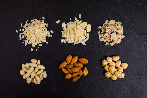 Vue de dessus de trois poignées de noix disposées sur un fond sombre Cacahuètes, amandes et noisettes sous forme entière et broyée