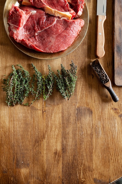 Vue de dessus de la viande fraîche crue à côté du romarin vert, des haricots au poivre et du couteau de chef. Table de cuisine.