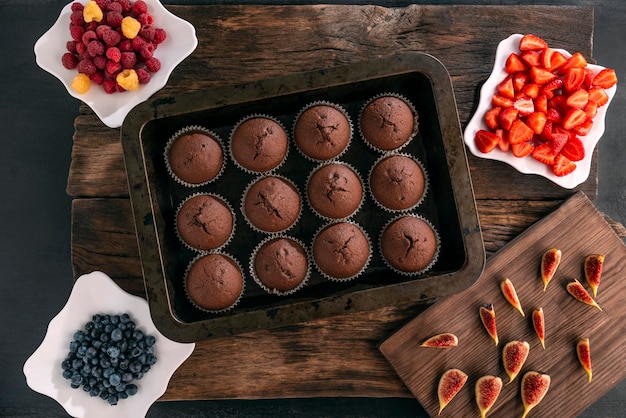 Vue de dessusPetits gâteaux au chocolat faits maison sur une plaque à pâtisserie Baies de saison pour la décoration Processus de fabrication de muffins aux fruits