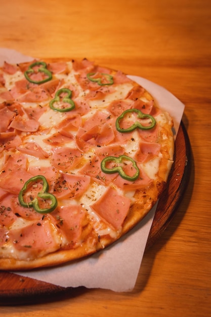 Vue détaillée d'une pizza au jambon et aux légumes sur une planche de bois