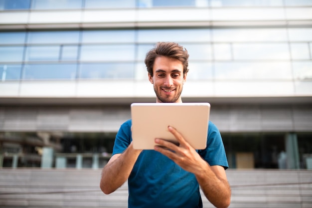 Vue de devant d'un jeune homme utilisant une tablette numérique à l'extérieur des immeubles de bureaux