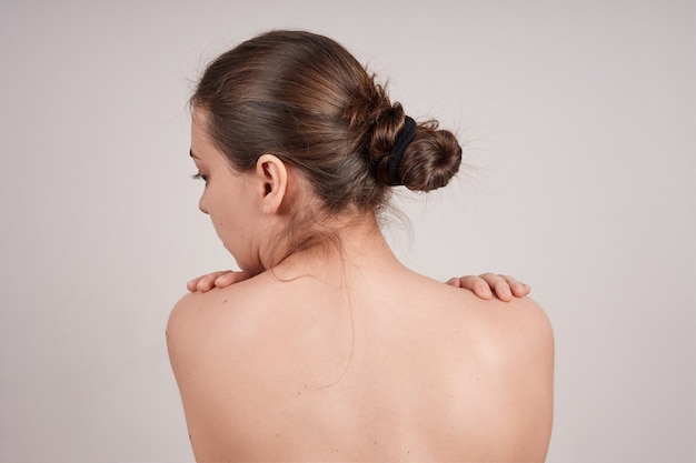 Vue de dos de jeune femme, épaules nues, tête de profil, isoler sur mur gris.