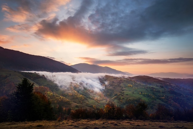 Vue du beau ciel nuageux sur la prairie à flanc de colline. Paysage majestueux de montagnes avec fumée et ciel lumineux dramatique sur fond. Concept de la nature et de l'aube.