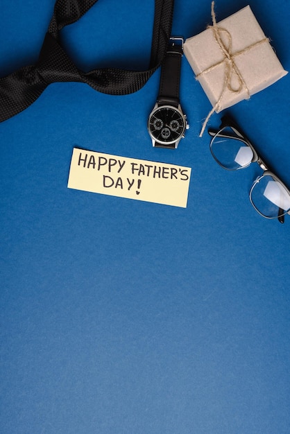 Vue du dessus de la carte de voeux de boîte-cadeau avec lettrage joyeux fête des pères accessoires pour hommes sur bleu