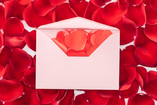 Vue du dessus de l'enveloppe avec des confettis en forme de coeur et des pétales de rose rouges sur fond saint valentin