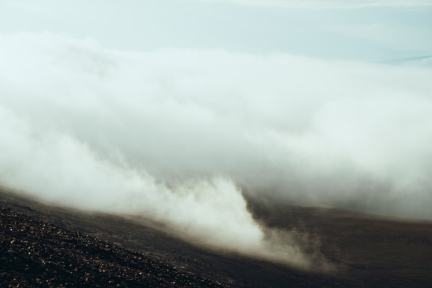 Vue du flanc de la montagne pierreuse à la vallée des hautes terres dans les nuages. Paysage alpin minimaliste sombre atmosphérique avec des nuages bas dans la vallée de la montagne. Magnifique paysage de montagne avec d'épais nuages au sol