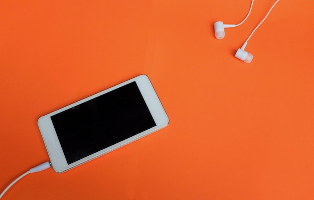 Vue du haut smartphone blanc et écouteurs sur fond orange