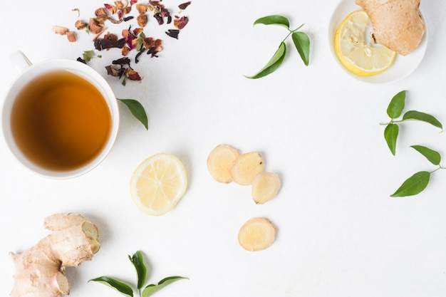 Une vue en élévation d&#39;une tasse de thé aux herbes avec du citron; herbes au gingembre et séchées sur fond blanc