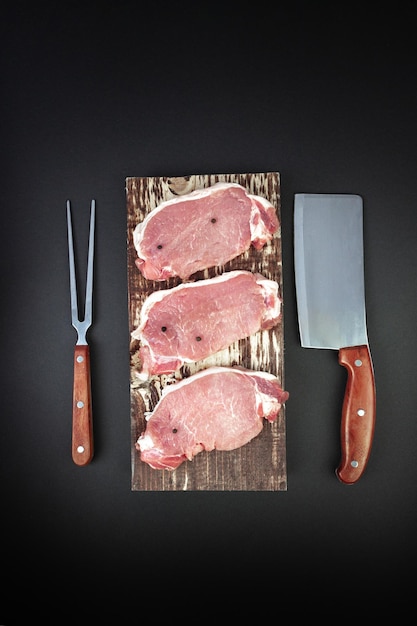 Vue élevée des steaks de viande crue et des épices dans la cuisine pour griller sur une planche à découper de cuisine avec des ingrédients pour la cuisson